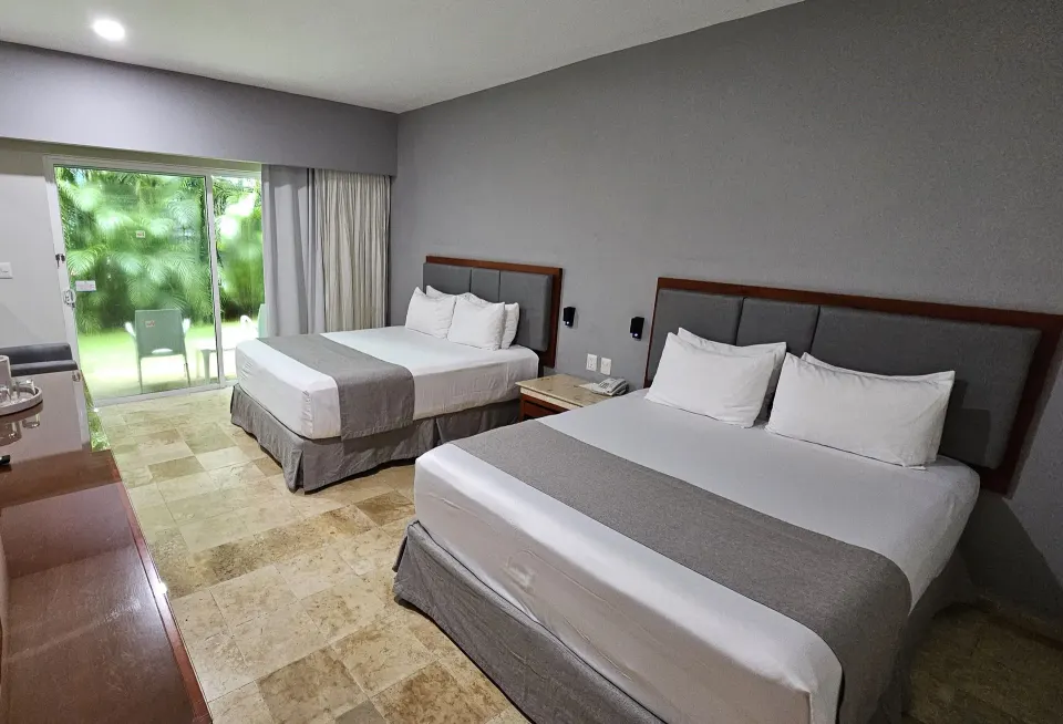 Standard guest room at Viva Maya showing two double beds and a patio door with greenery outside.
