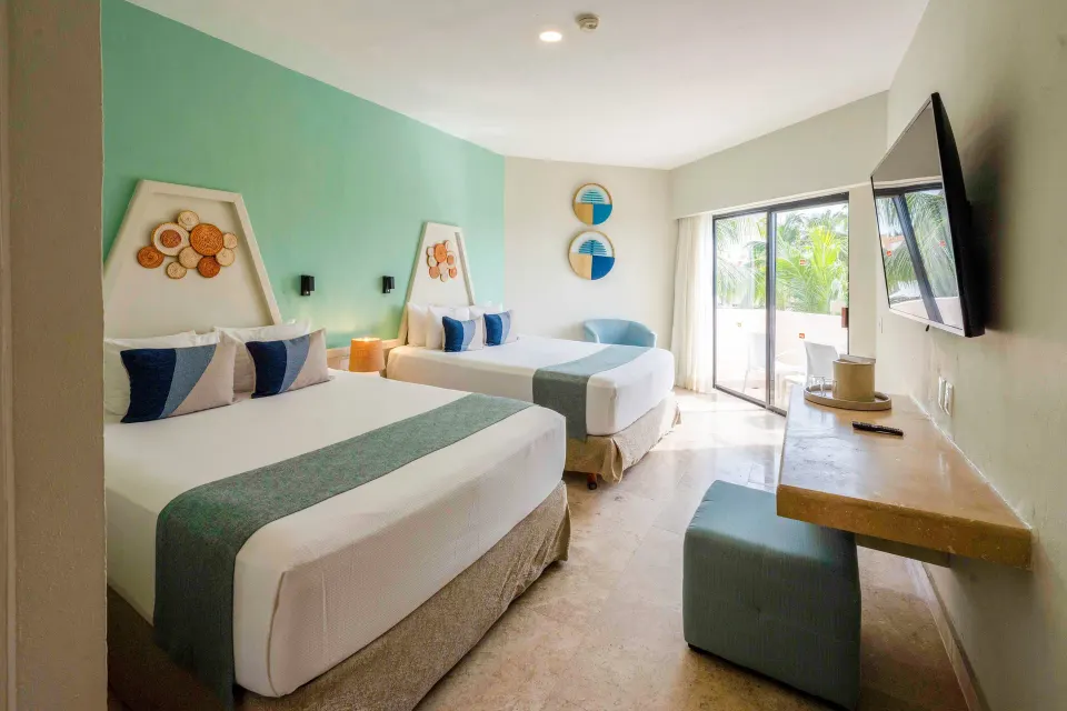 Two queen beds aligned toward a patio door in a Viva Maya guest room
