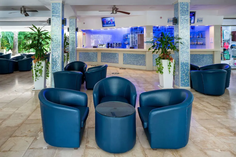 Casual indoor bar area at Viva Maya with blue lounge chairs and a backlit service counter.