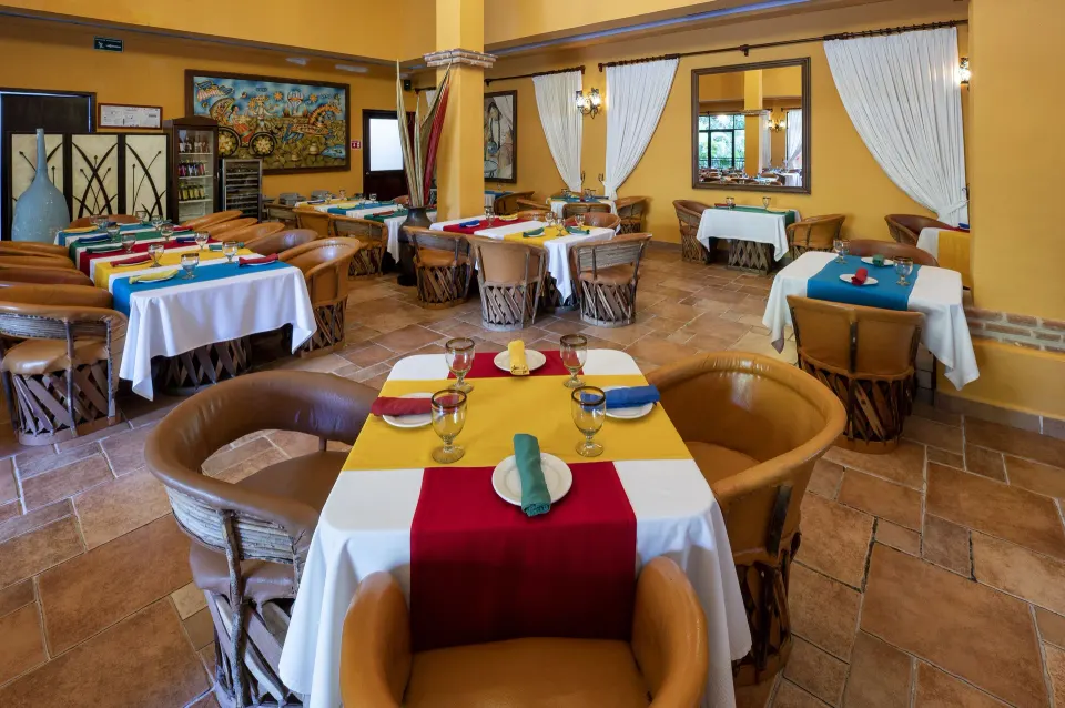 Hacienda dining room with small round tables and colorful napkins at Viva Maya