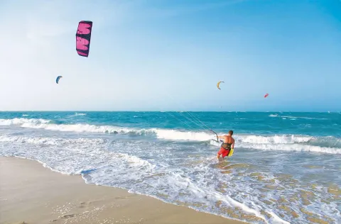 Kitesurfer entering the ocean from a sandy beach at Viva Tangerine.