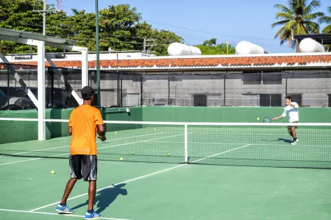 Two people practicing tennis on an outdoor green court at Viva Tangerine.
