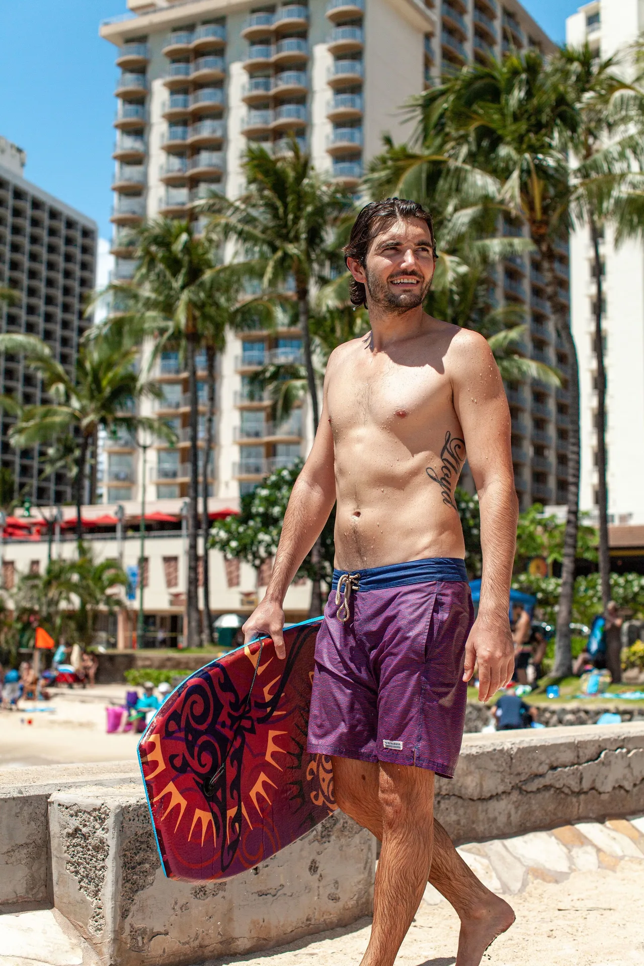 Man holding a bodyboard near the beach and palms by Vive Hotel Waikiki.