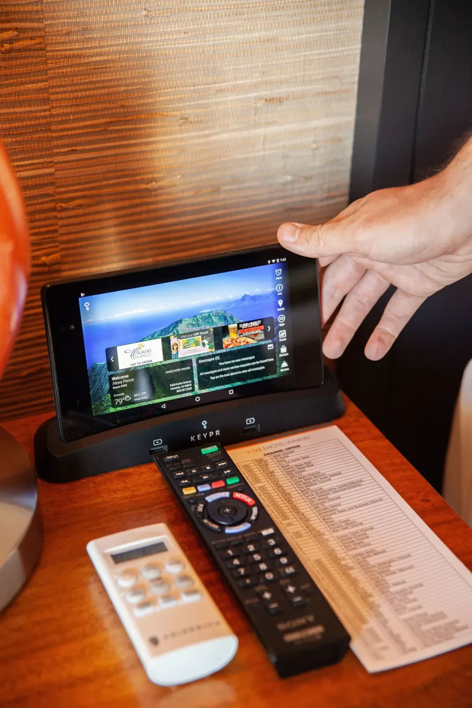 Bedside tablet, remotes, and printed guide on a nightstand at Vive Hotel Waikiki.