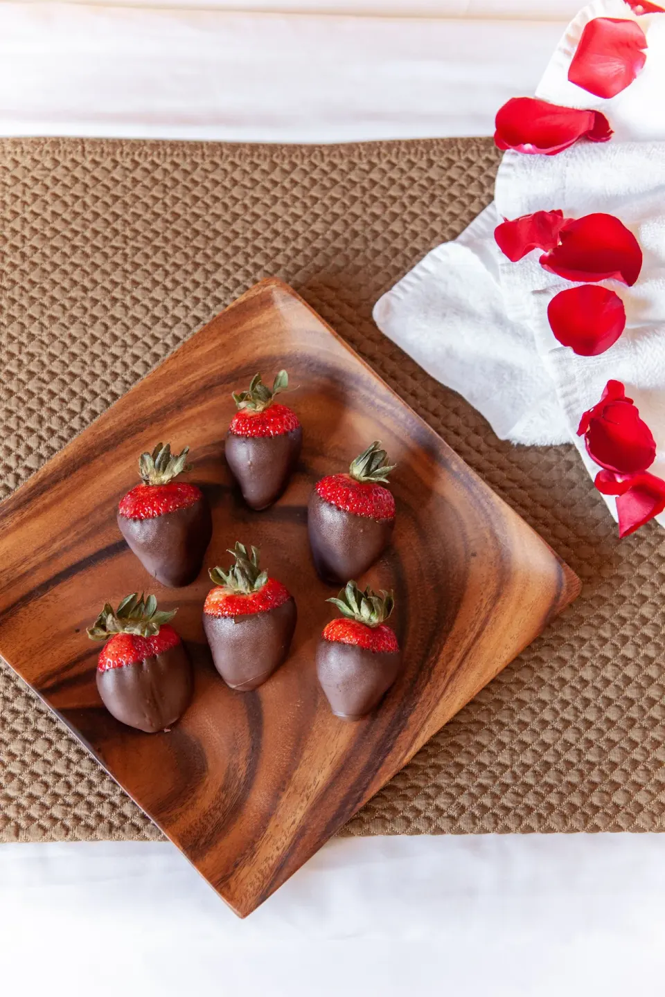Chocolate-covered strawberries and rose petals on a bed at Vive Hotel Waikiki.