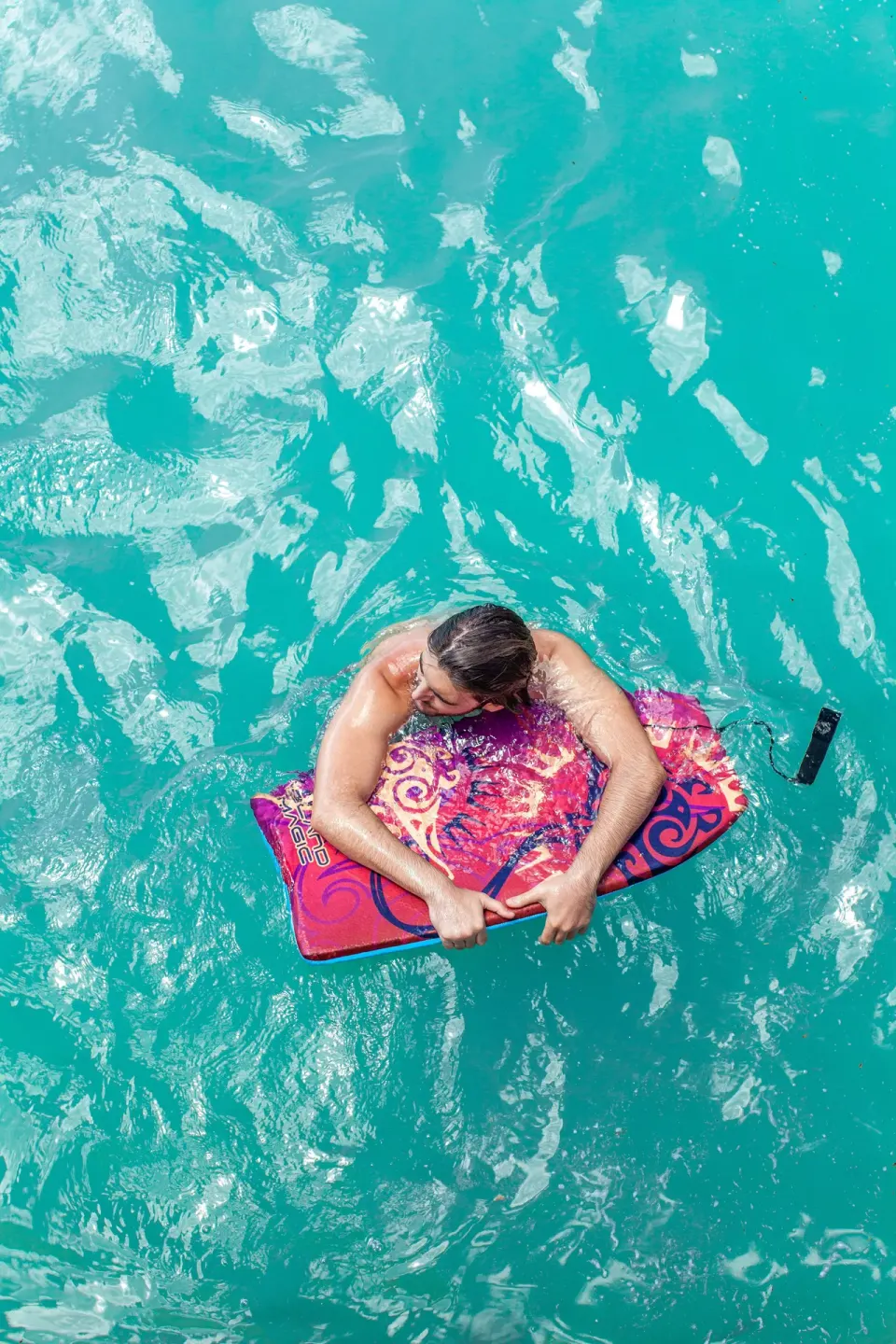 Guest floating on a pink mat in turquoise water at Vive Hotel Waikiki.