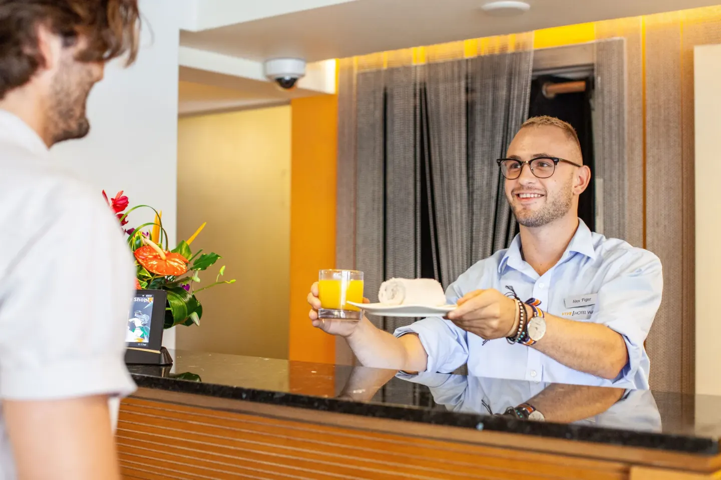 A front desk attendant hands a drink and rolled towel to a guest at Vive Hotel Waikiki.