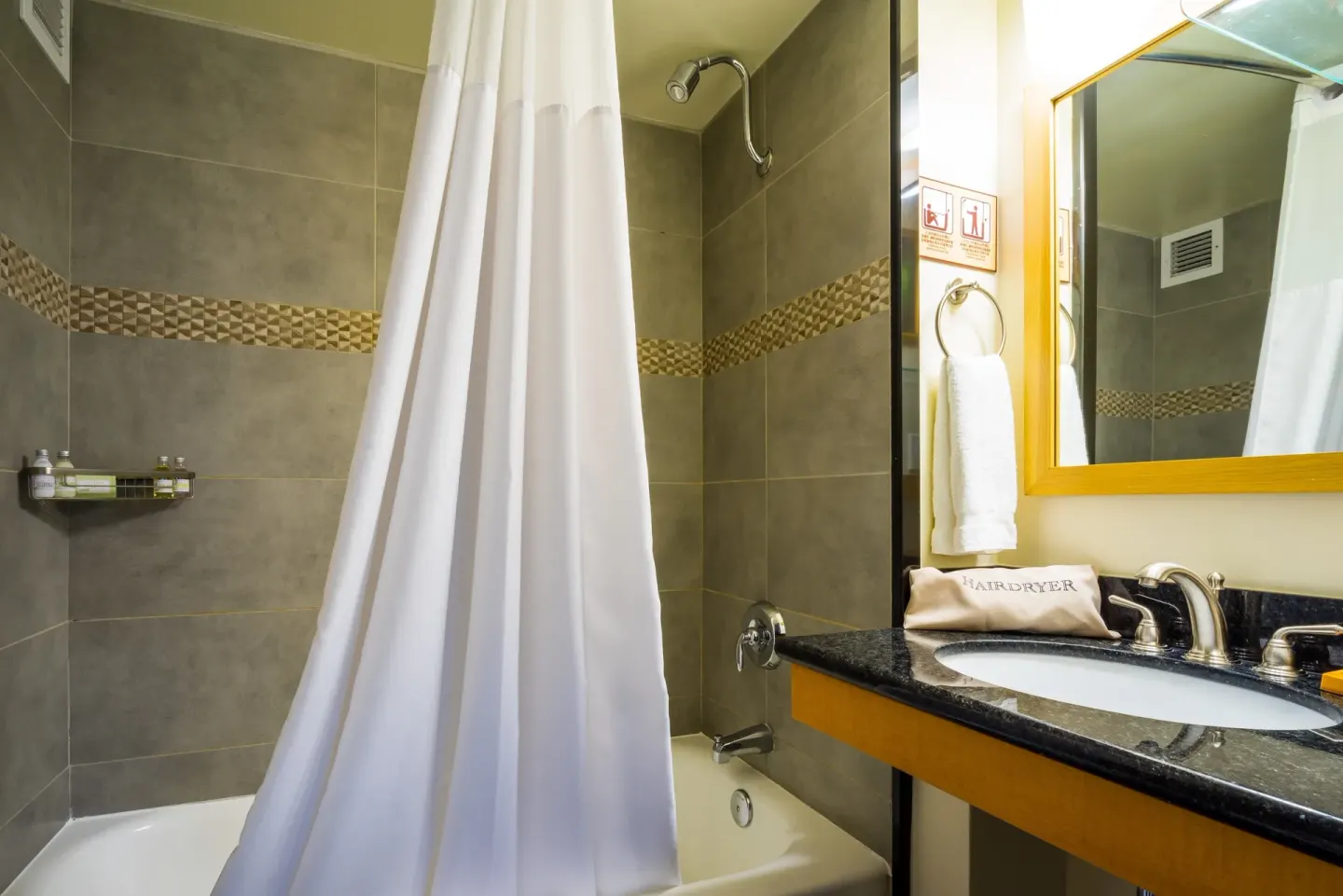 Bathroom with tub, shower curtain, vanity, and mirror at Vive Hotel Waikiki.