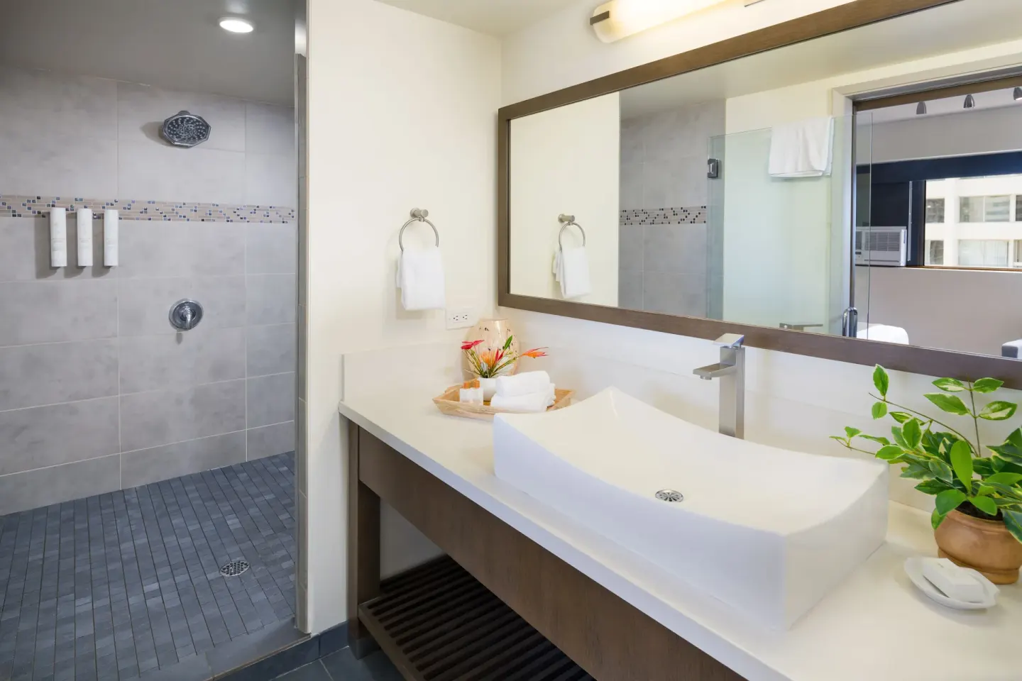 Guest bathroom with walk-in shower, vessel sink, and large mirror at Vive Hotel Waikiki.