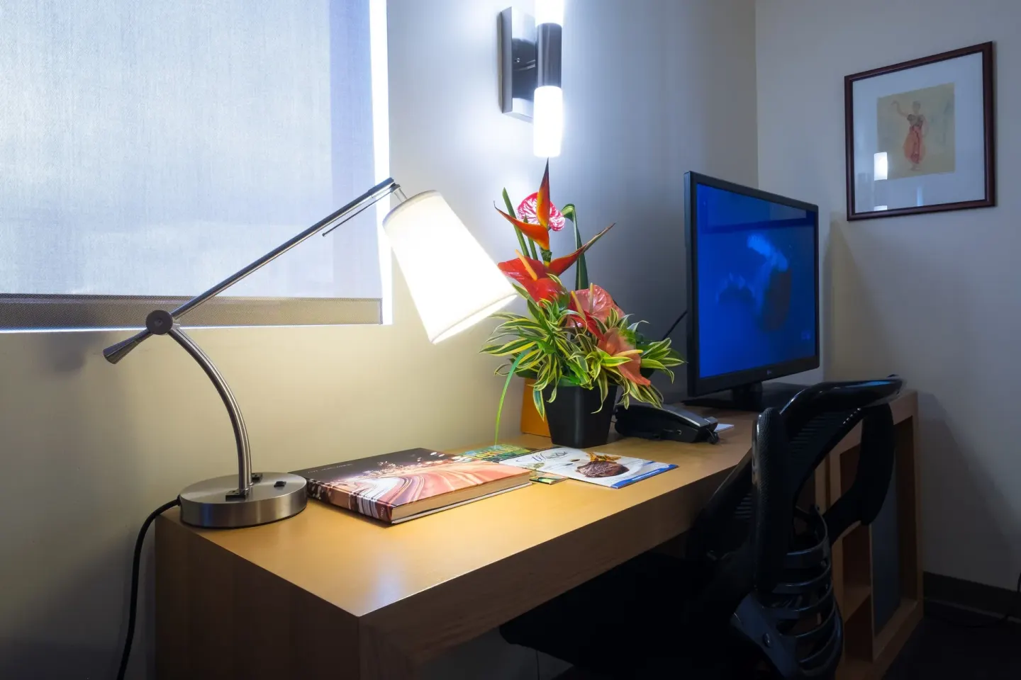 Guest room desk with lamp, flowers, and television at Vive Hotel Waikiki.
