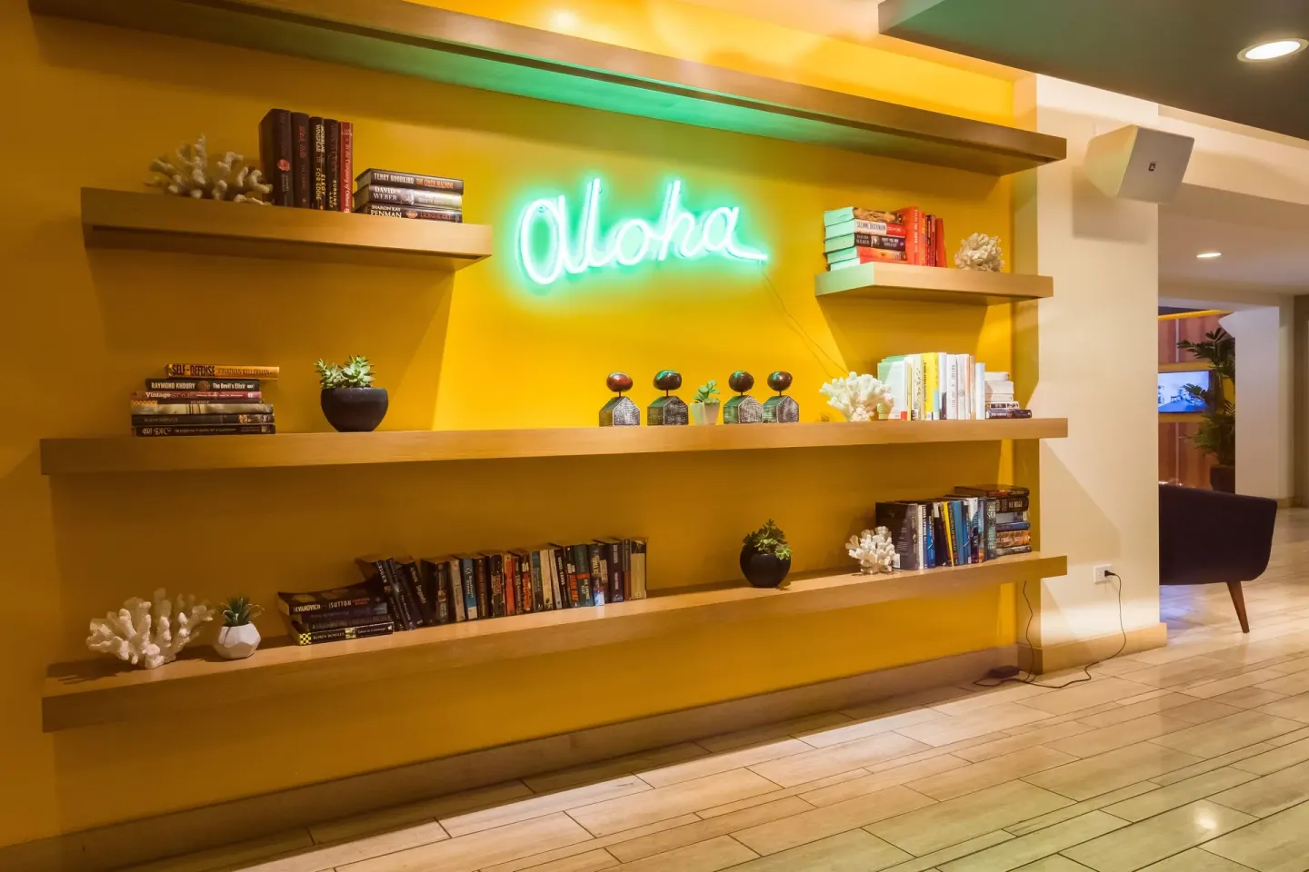 Lobby shelving with books, decor, and a neon aloha sign at Vive Hotel Waikiki.