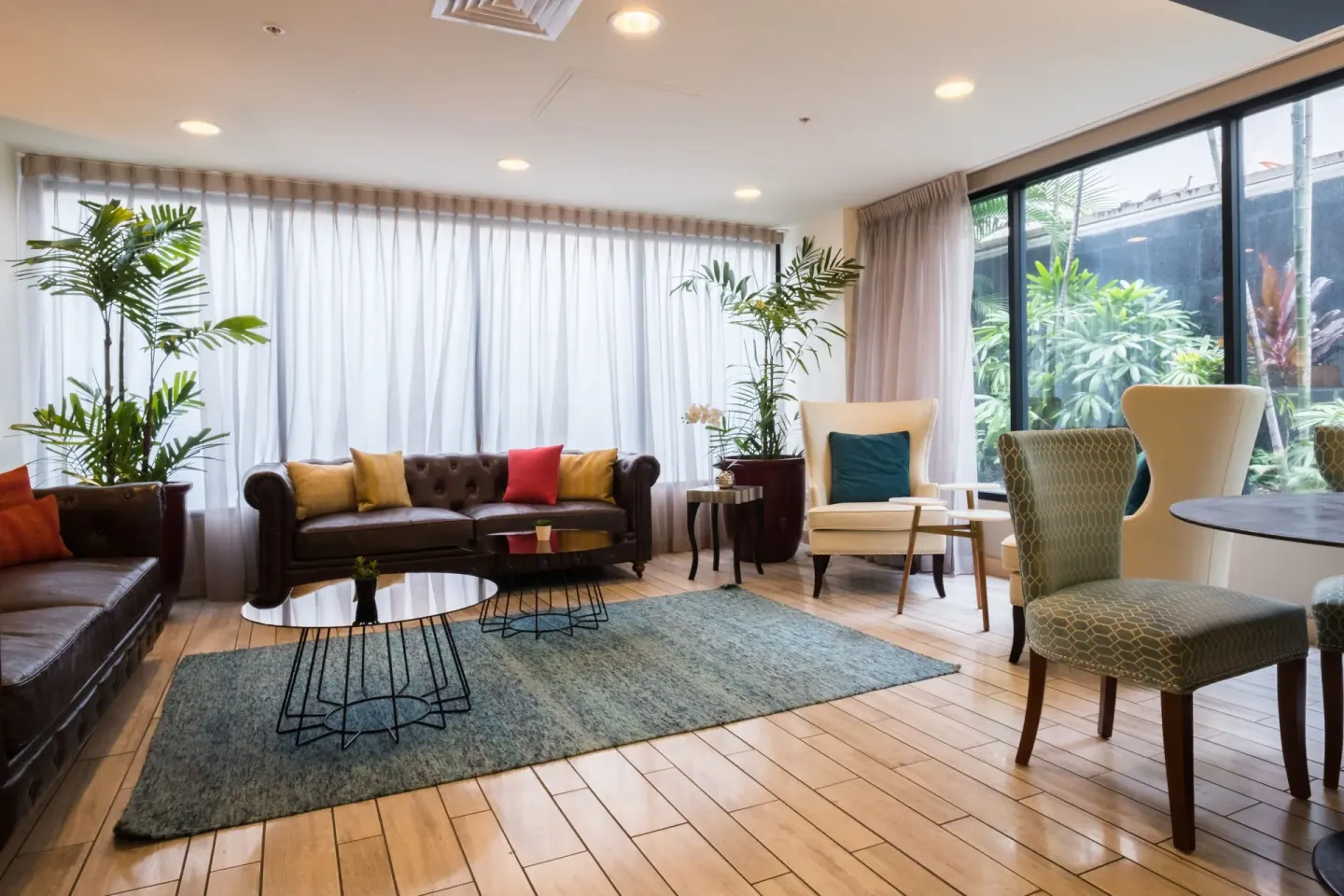 Lobby lounge with sofas, chairs, plants, and garden windows at Vive Hotel Waikiki.