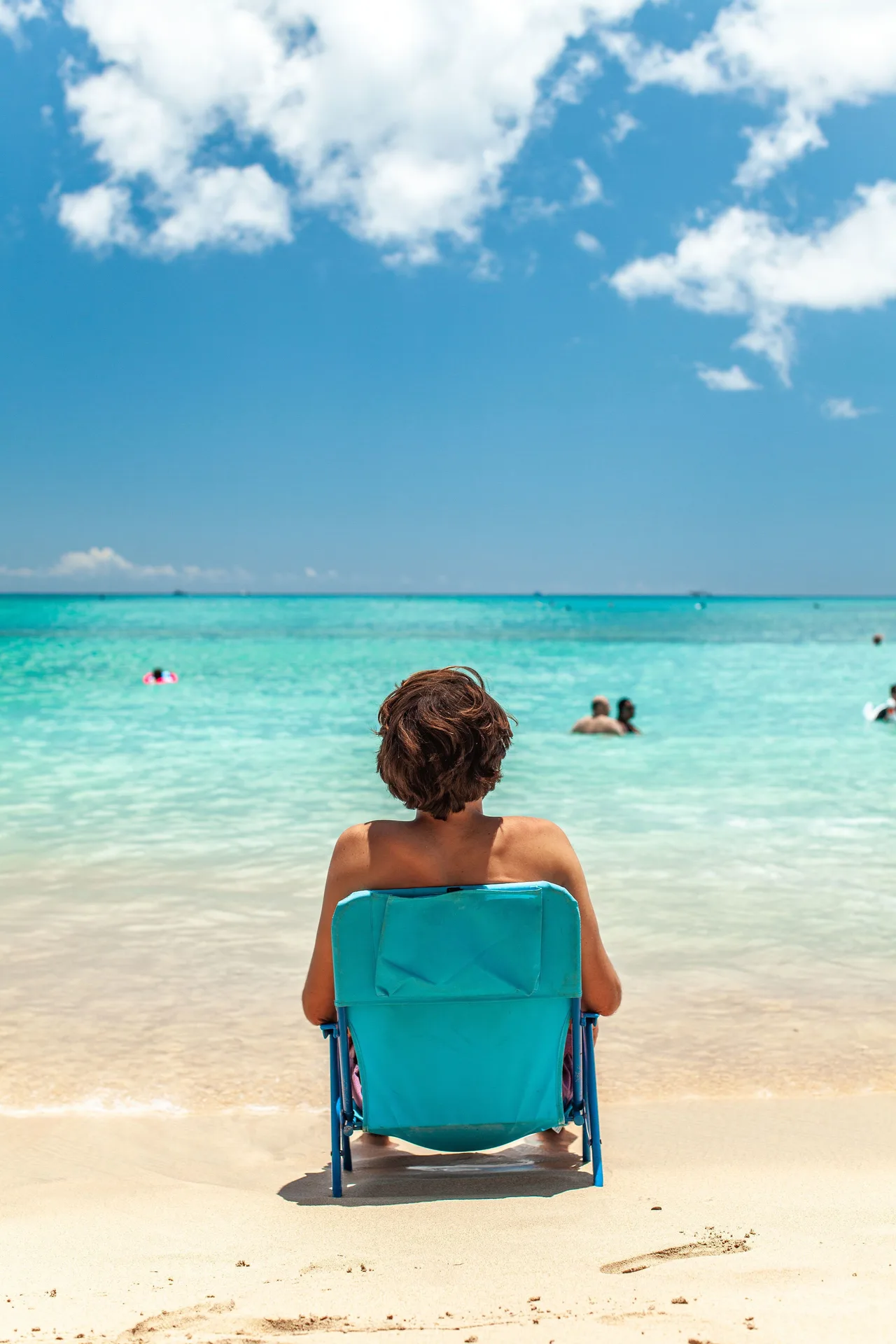 Person seated in a blue beach chair facing the ocean near Vive Hotel Waikiki.