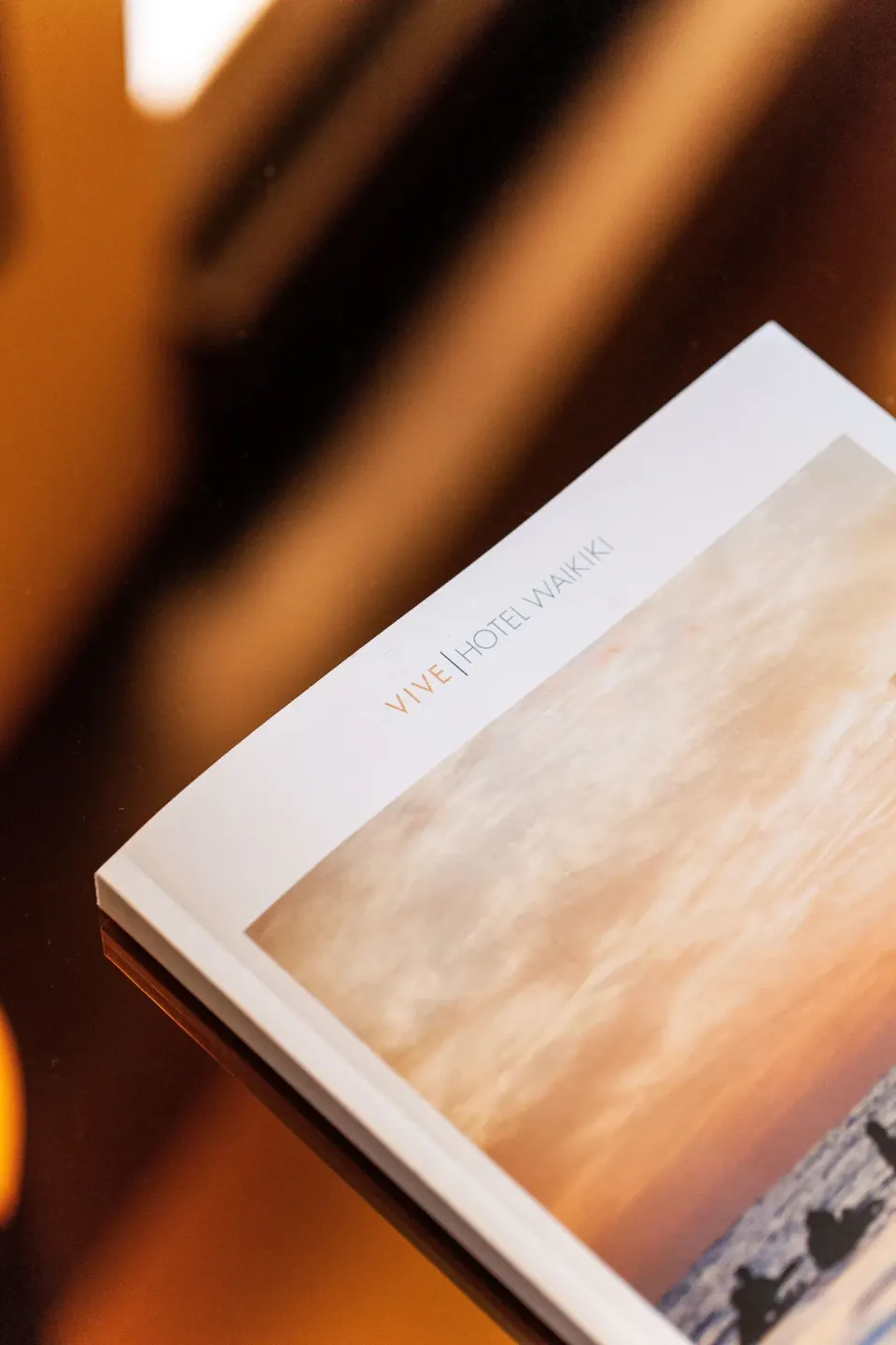 Printed Vive Hotel Waikiki card or booklet on a glossy table in warm light.