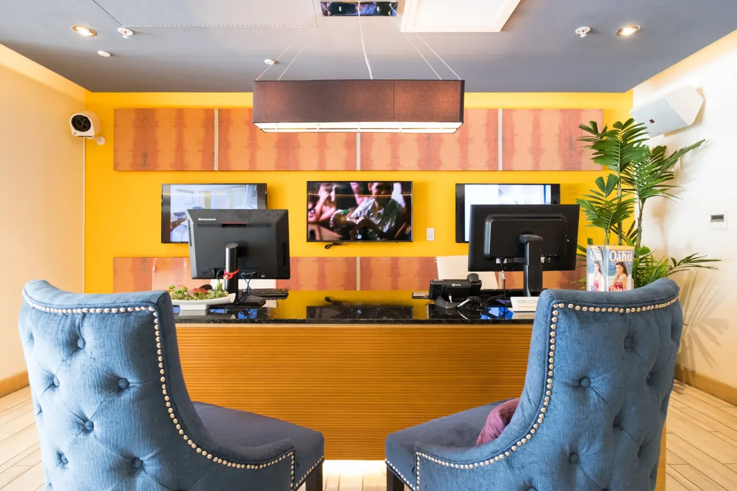 Reception desk with blue chairs and yellow wall at Vive Hotel Waikiki.