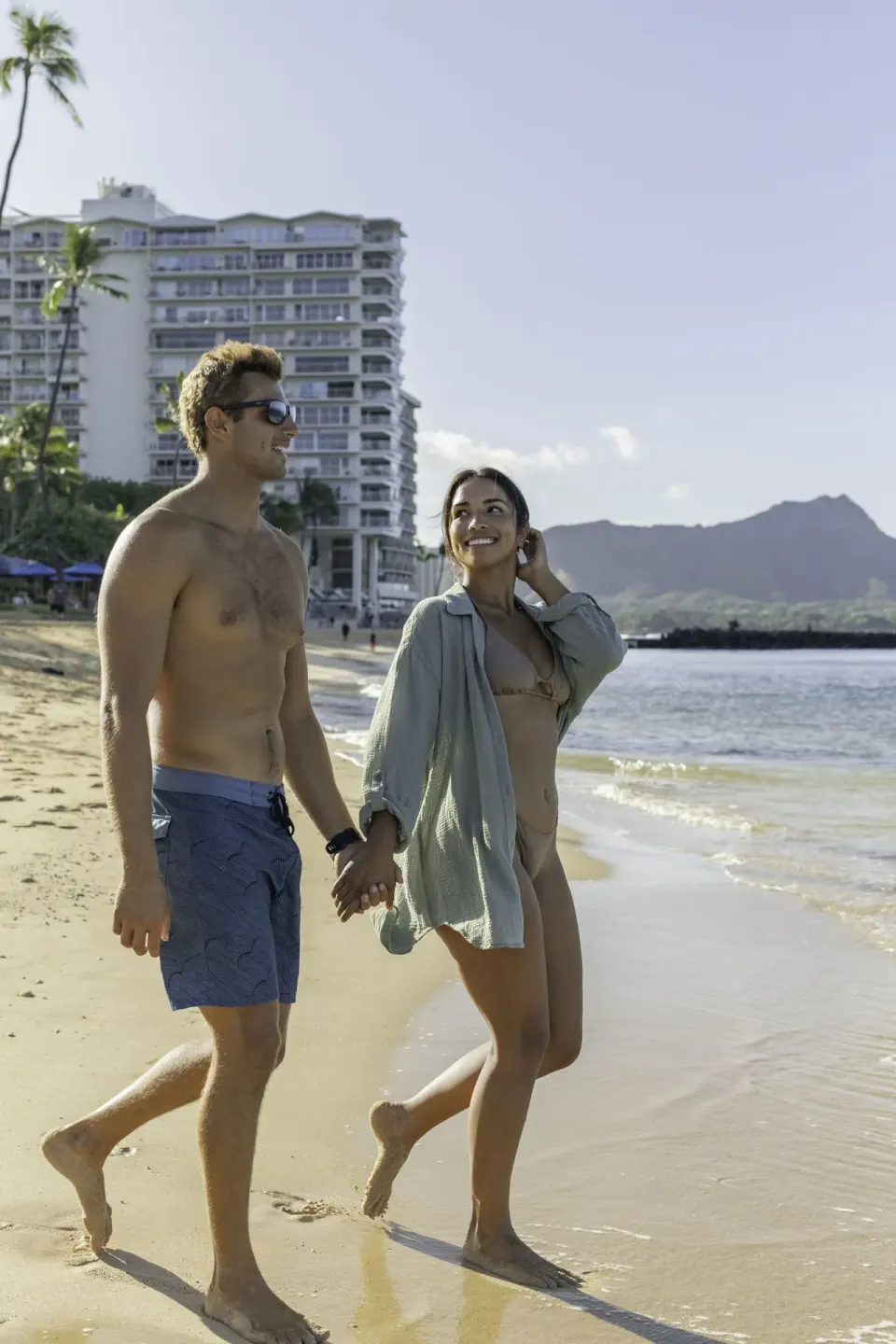 Two guests walk along Waikiki Beach near the water by Vive Hotel Waikiki.