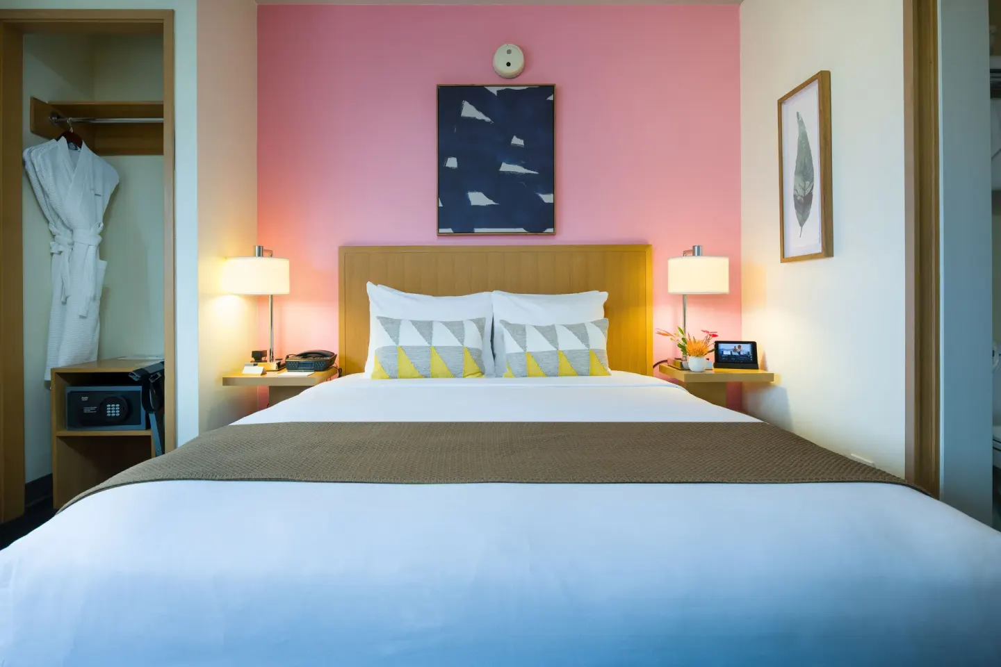 King bed in a Deluxe Ocean View room with pink accent wall at Vive Hotel Waikiki.