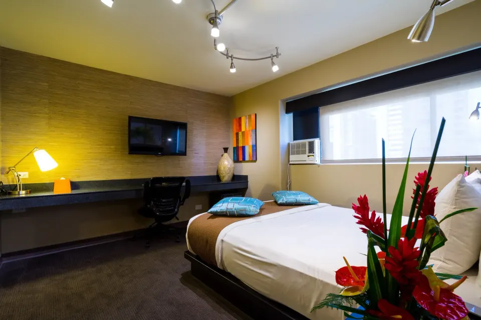 Bed, window, and desk in a Lifestyle Family Suite City View room at Vive Hotel Waikiki.