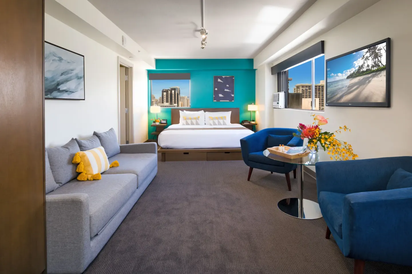 Lifestyle Jr. Suite with king bed, sofa, blue chairs, and city windows at Vive Hotel Waikiki.