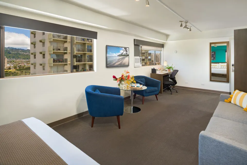 Lifestyle Jr. Suite with sofa, blue chairs, desk, and mountain-view windows at Vive Hotel Waikiki.