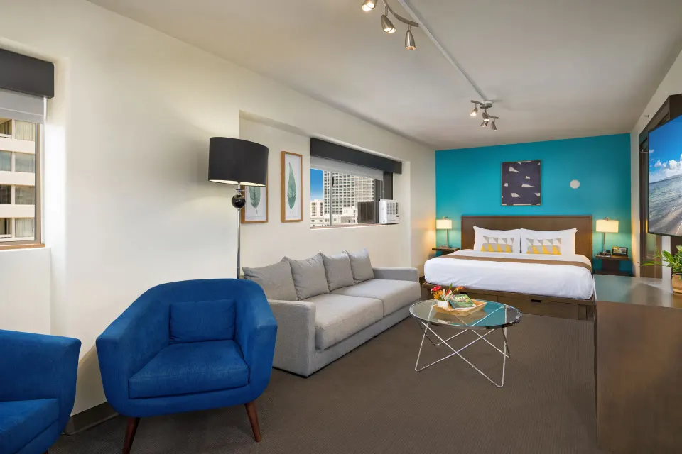 Lifestyle Jr. Suite with king bed, gray sofa, and blue chairs at Vive Hotel Waikiki.