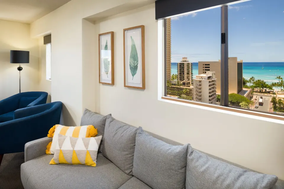 Gray sofa beneath ocean-view windows in a Lifestyle Jr. Suite at Vive Hotel Waikiki.