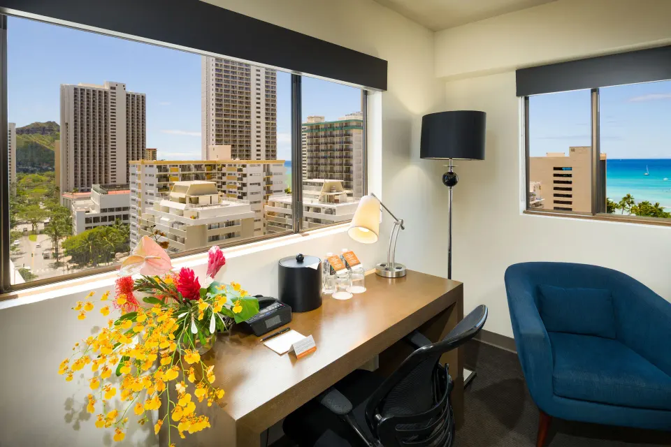 Work desk and blue chair with city and ocean views in a suite at Vive Hotel Waikiki.