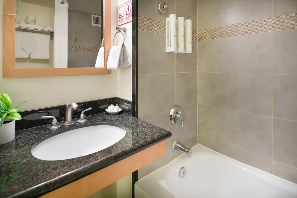 Standard Room bathroom vanity and tiled bathtub at Vive Hotel Waikiki.
