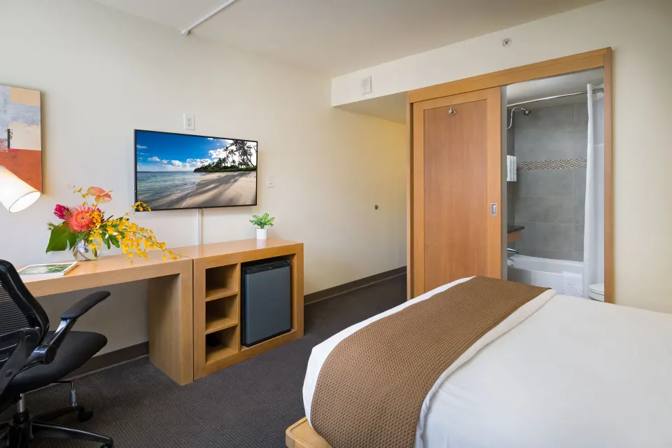 Standard Room with bed, desk, TV and bathroom doorway at Vive Hotel Waikiki.