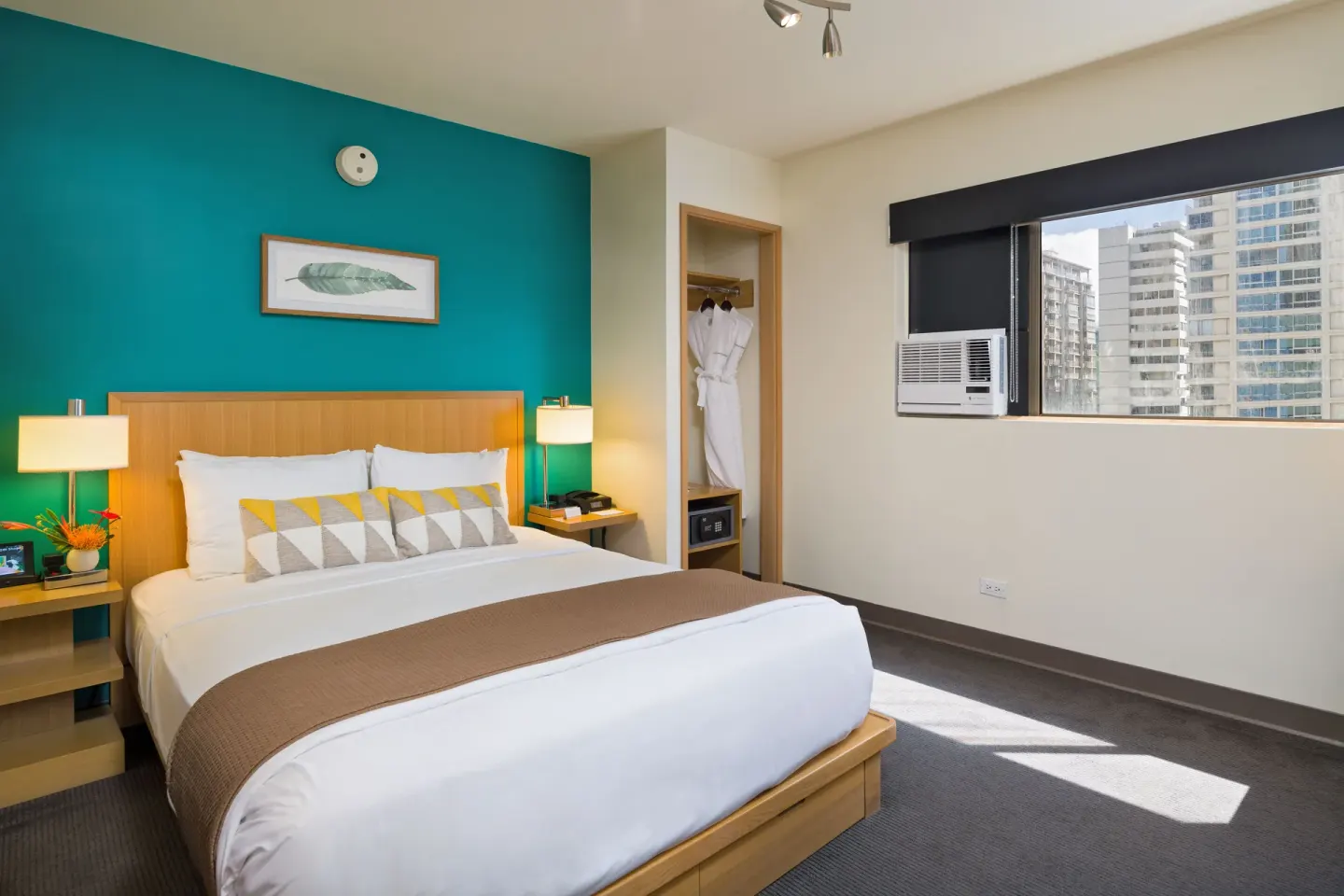 Standard Room with queen bed, teal wall and city-facing window at Vive Hotel Waikiki.