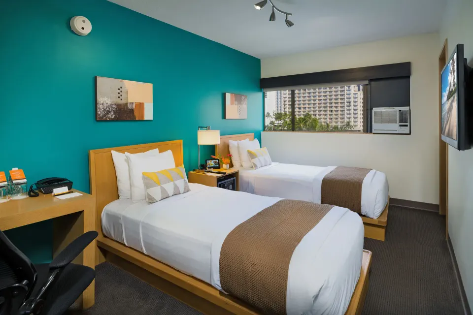 Two twin beds, desk, and city window in a Standard Room at Vive Hotel Waikiki.