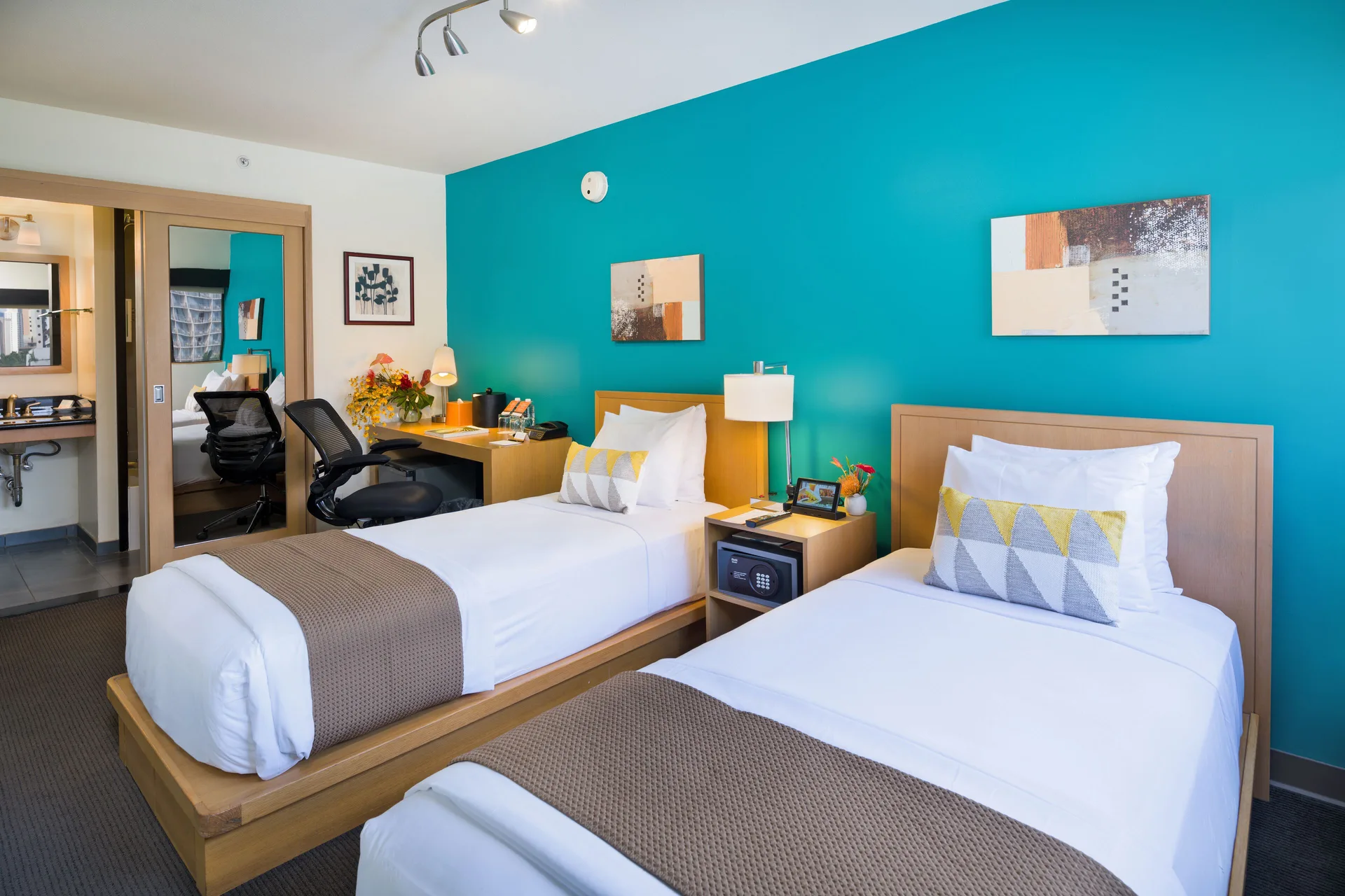 Two twin beds with a teal accent wall in a Standard Room at Vive Hotel Waikiki.