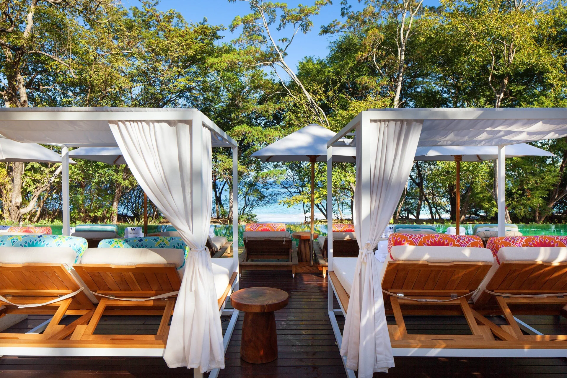 Beach cabanas with loungers, curtains, and ocean glimpses at W Costa Rica - Reserva Conchal.