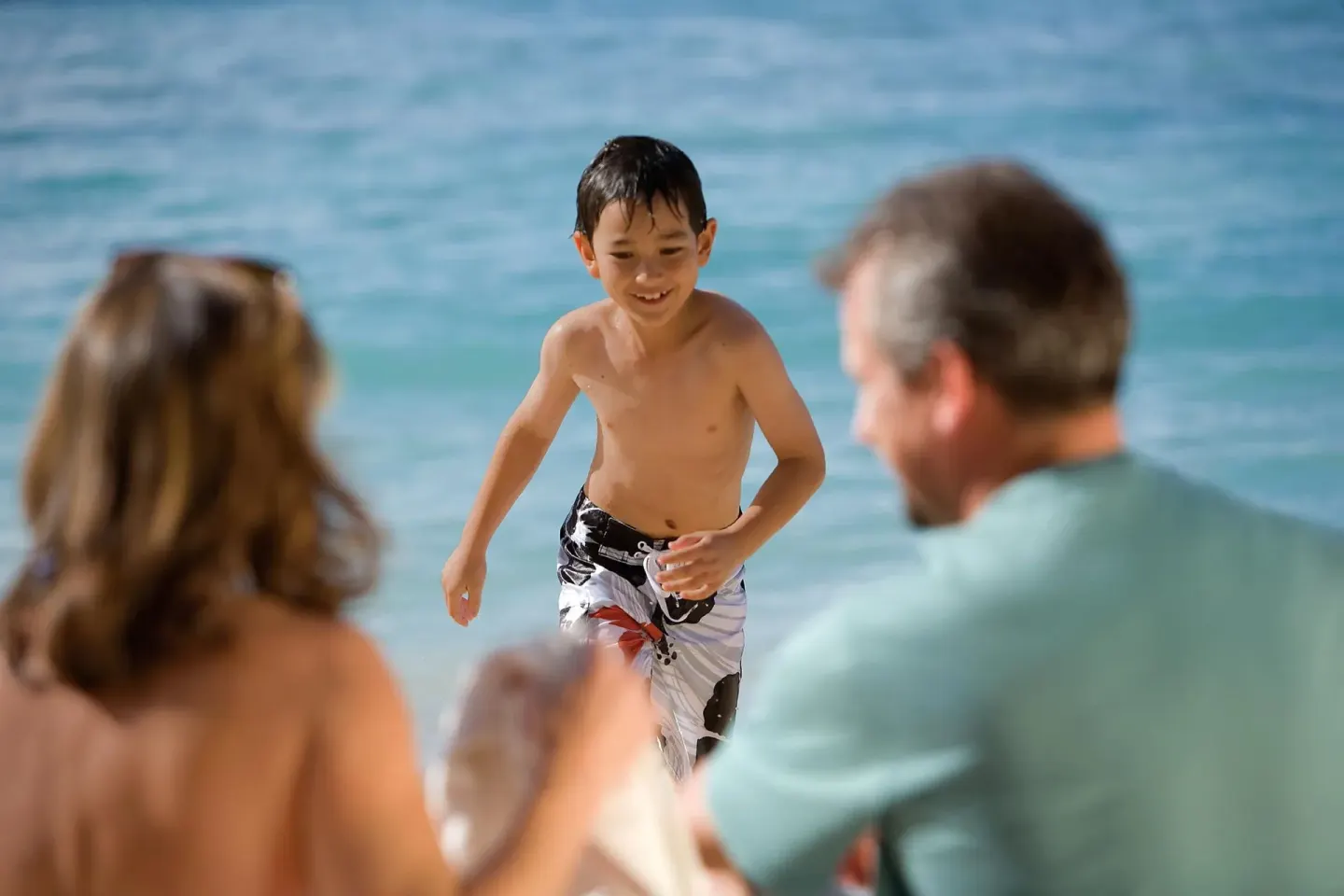 A child runs from the surf toward family on the beach at W Costa Rica - Reserva Conchal.