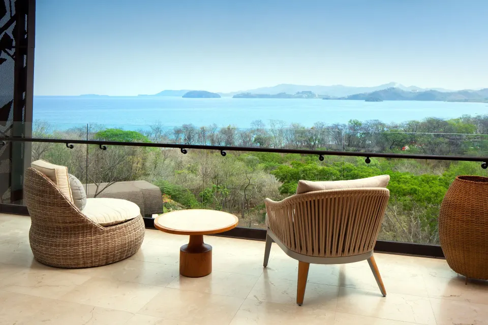 Premier Room Ocean View balcony with chairs, table and bay panorama at W Costa Rica - Reserva Conchal.