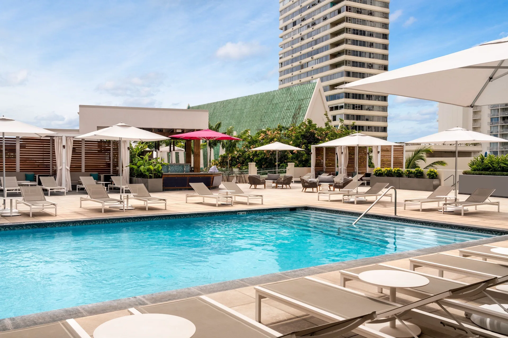 Sunny pool deck with loungers, umbrellas and cabanas at Waikiki Beach Marriott Resort & Spa.