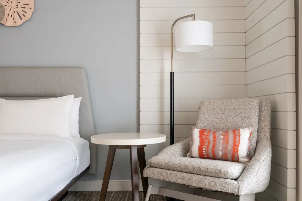 Guest room seating area at Waikiki Beach Marriott Resort & Spa with bed, chair, table, and floor lamp.