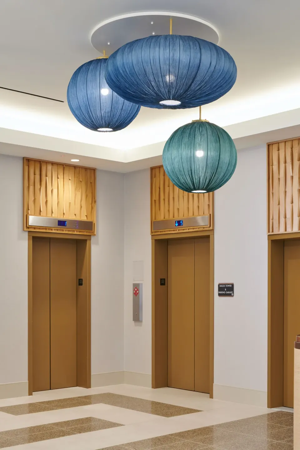 Elevator lobby with gold doors and blue pendant lights at Waikiki Malia.