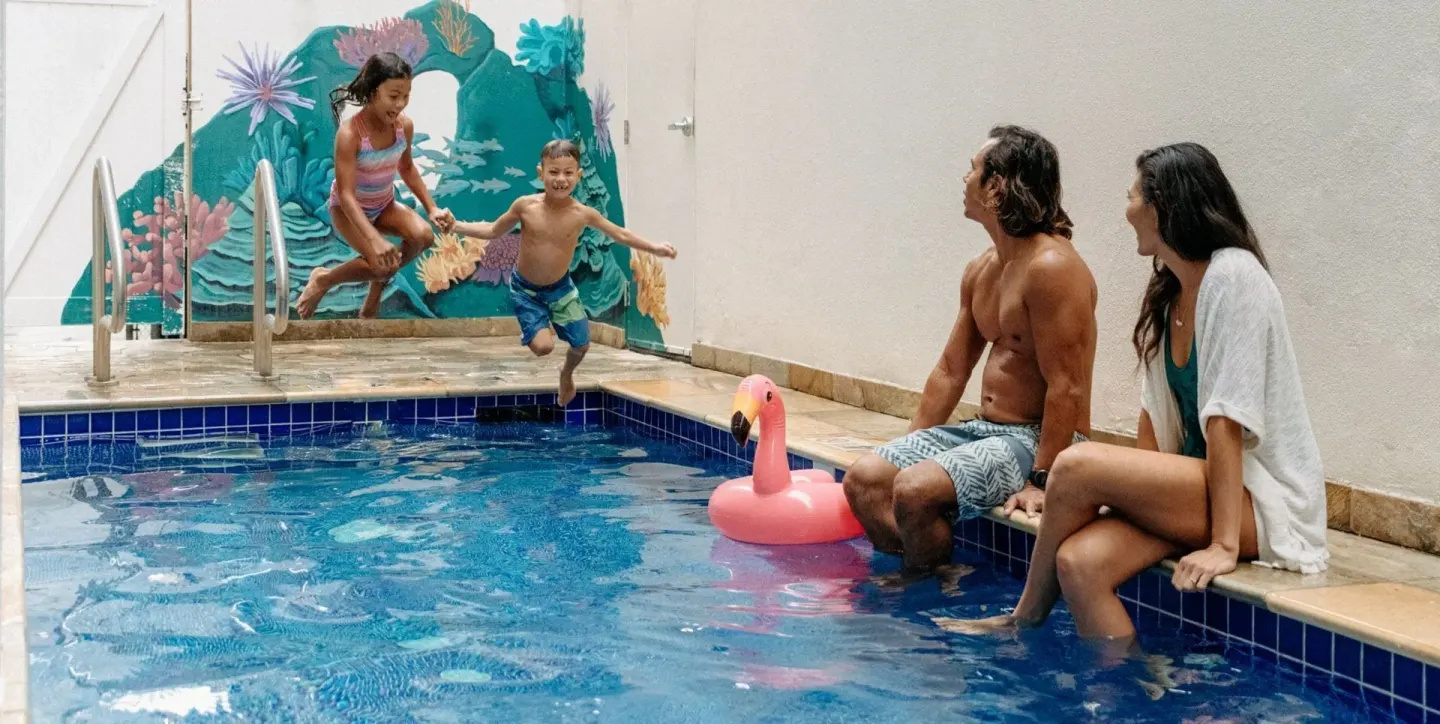 Children jump into the pool while parents sit nearby at Waikiki Malia.