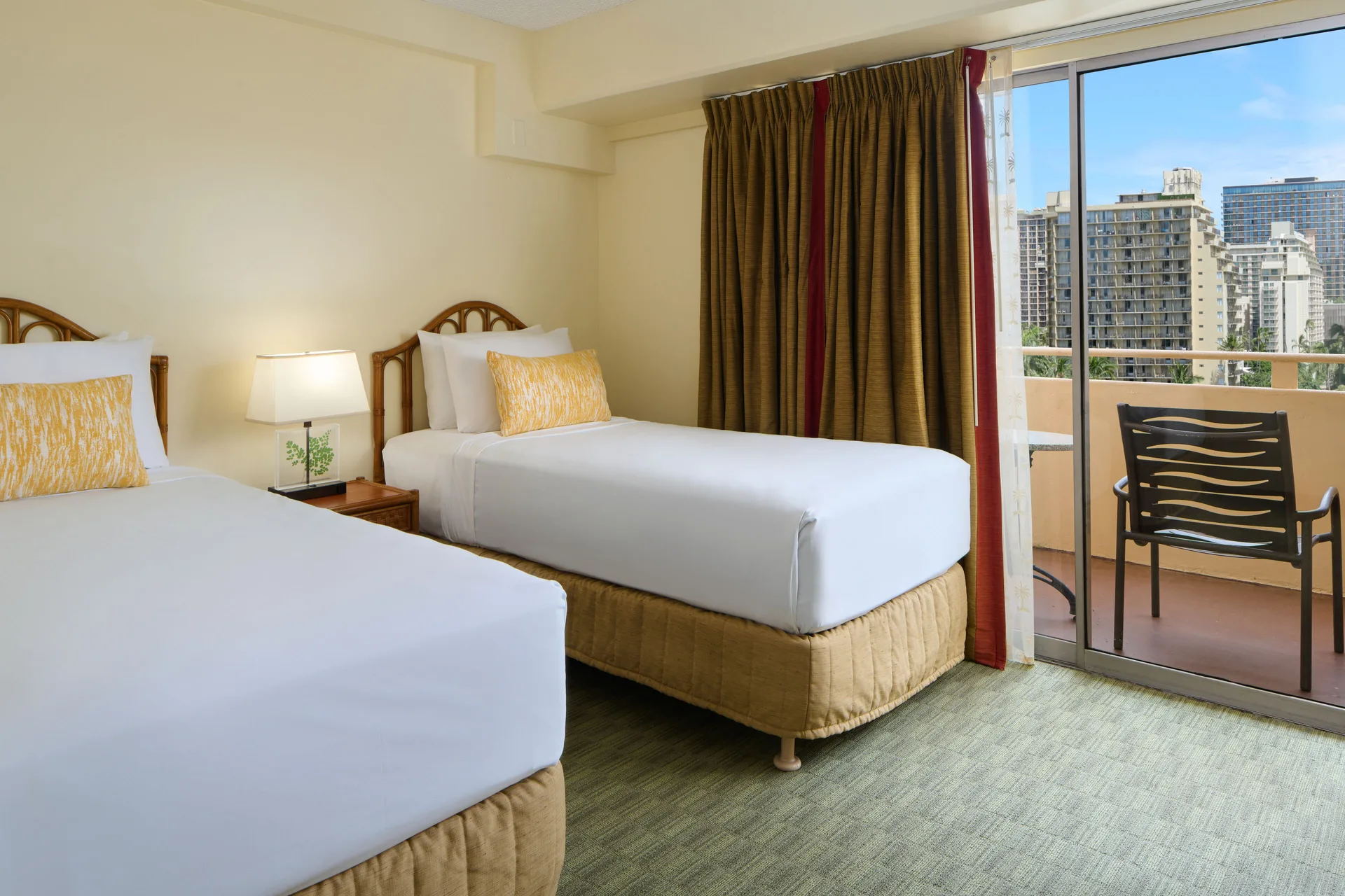 Guest room with two beds, balcony, and city buildings visible at Waikiki Malia.