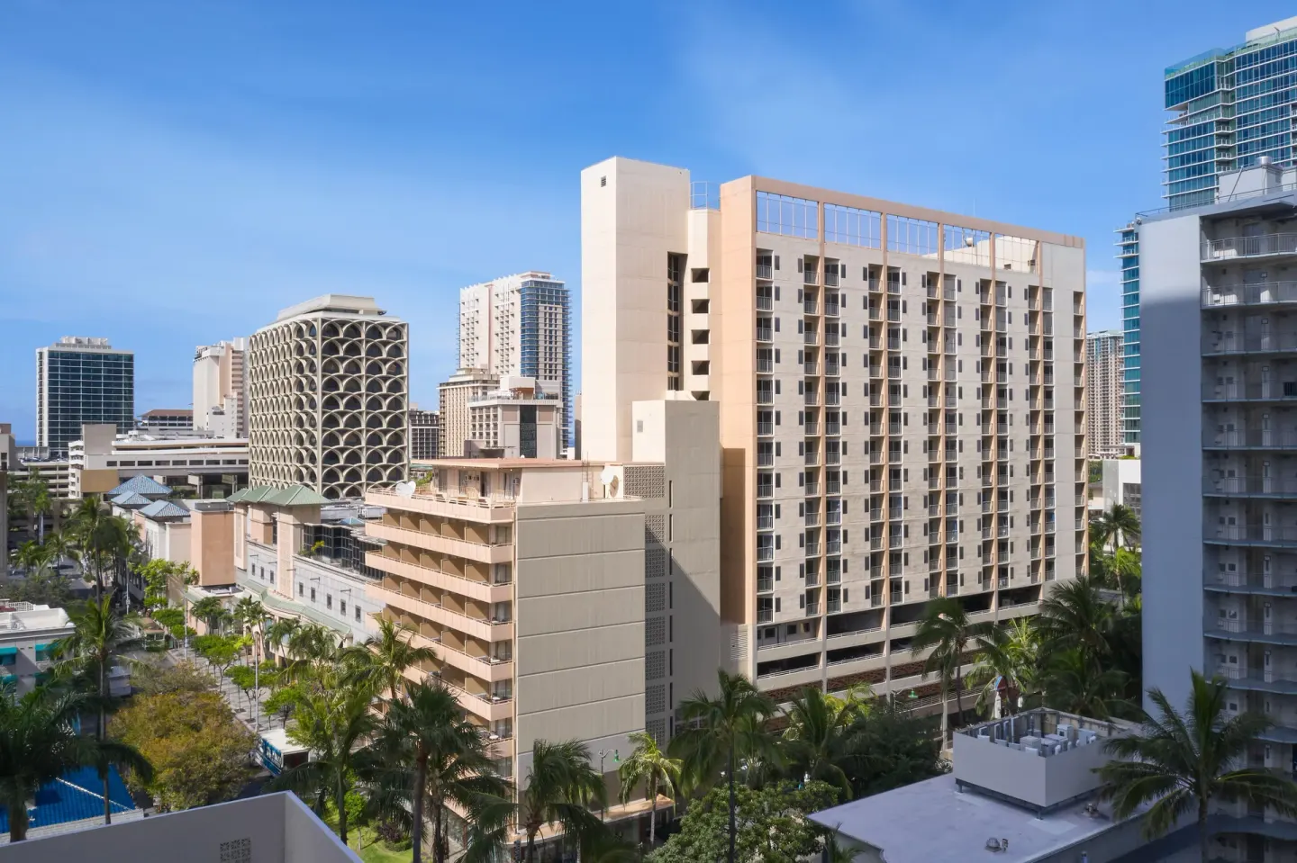 Waikiki Malia exterior rises among palm trees and neighboring city buildings.