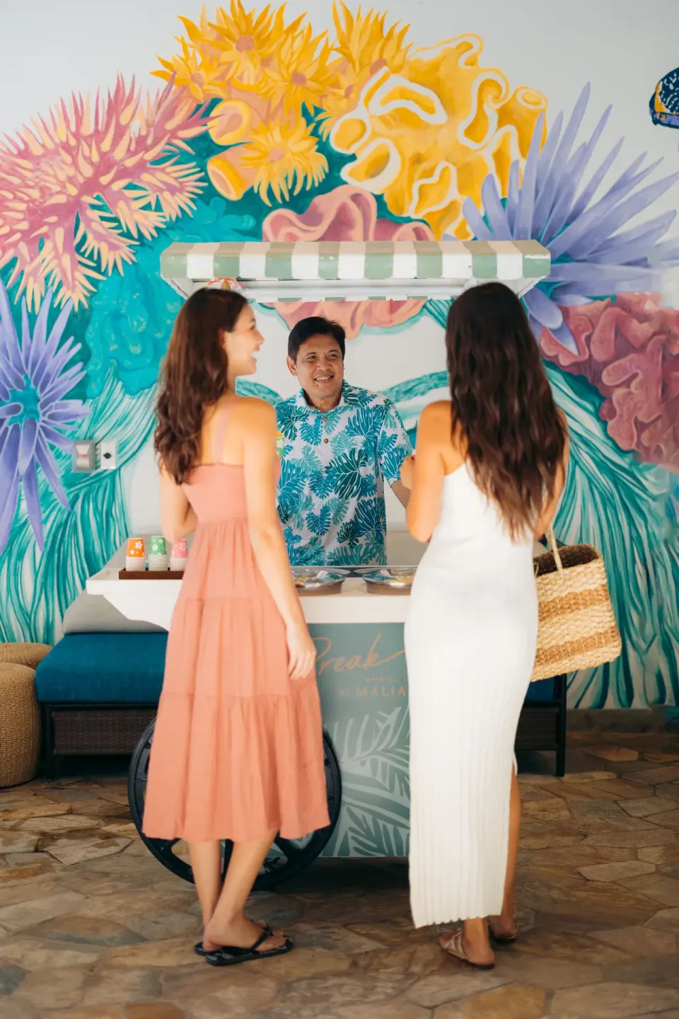 Guests at a small refreshment cart in front of a colorful mural at Waikiki Malia.