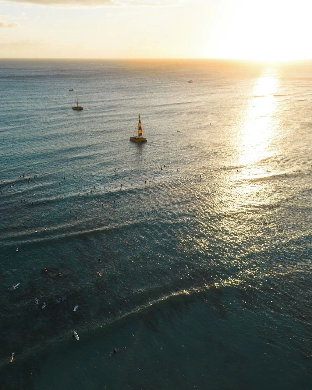 Sunset over the ocean with surfers and sailboats near Waikiki Malia.