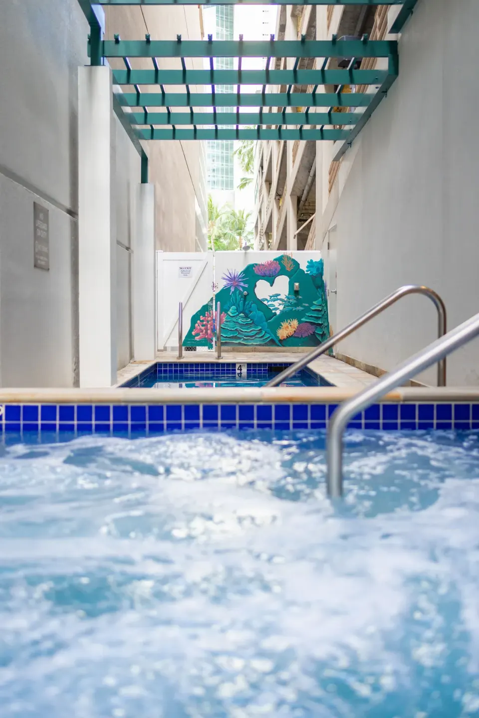 A pool and bubbling spa sit beneath a teal overhead trellis at Waikiki Malia.