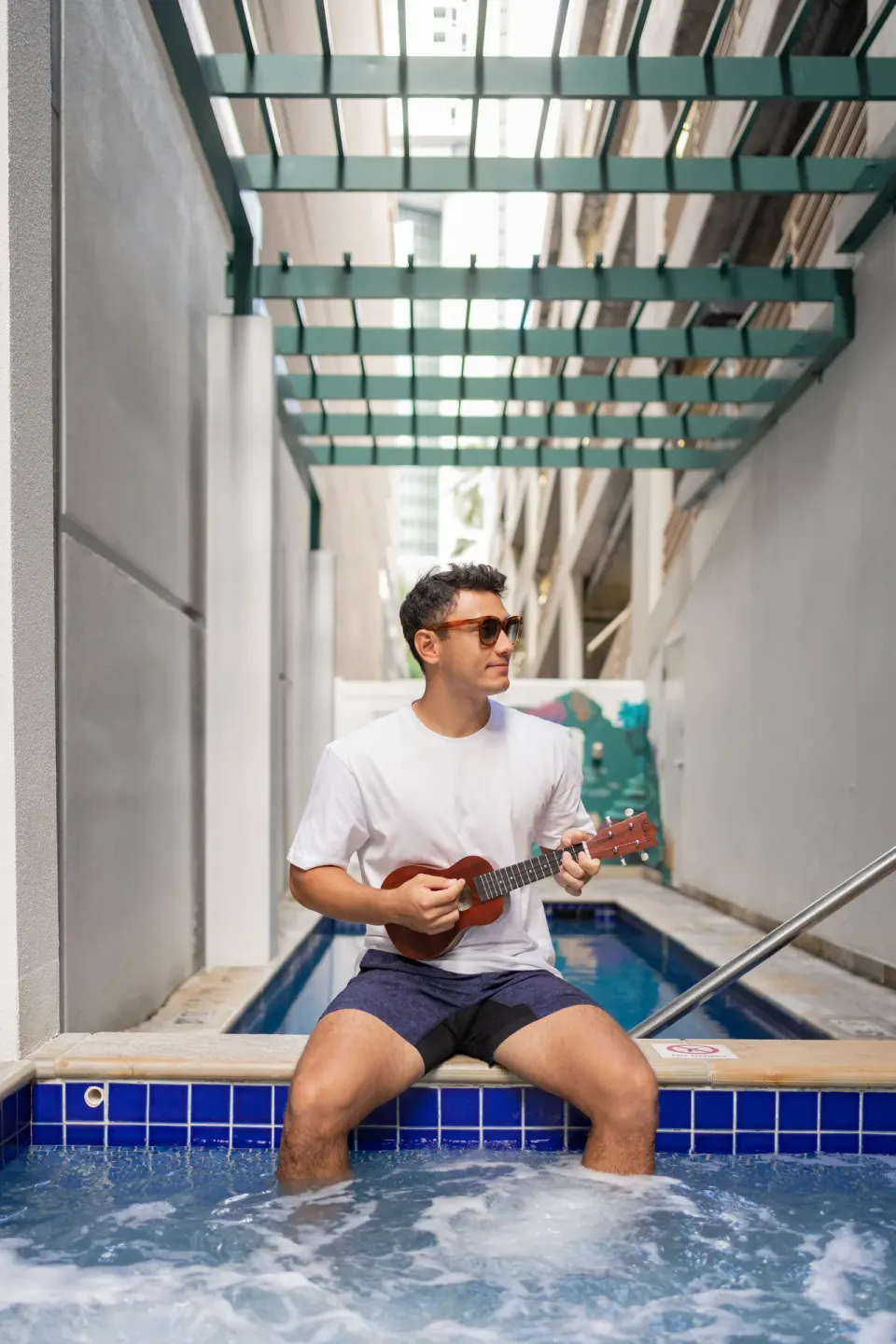 A guest plays a ukulele beside the hot tub and pool area at Waikiki Malia.