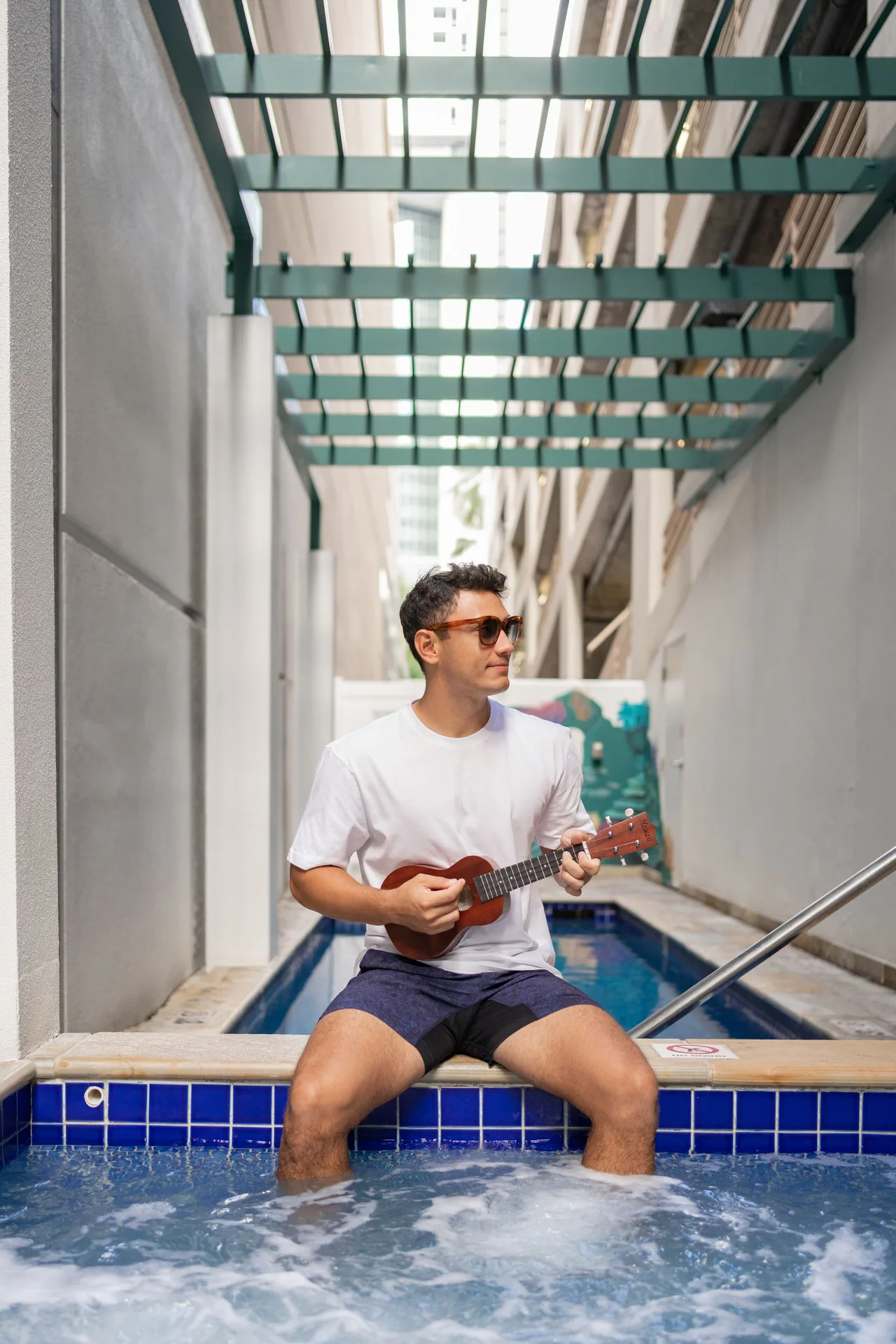 A guest plays a ukulele beside the hot tub and pool area at Waikiki Malia.