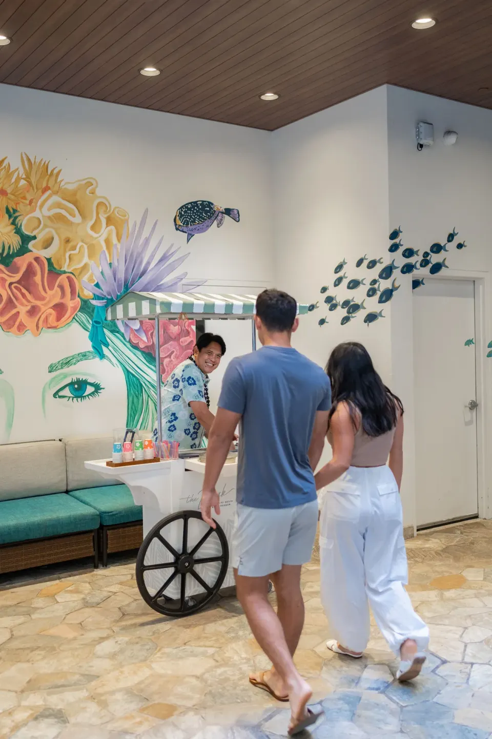 Guests approach a refreshment cart by a tropical mural at Waikiki Malia.