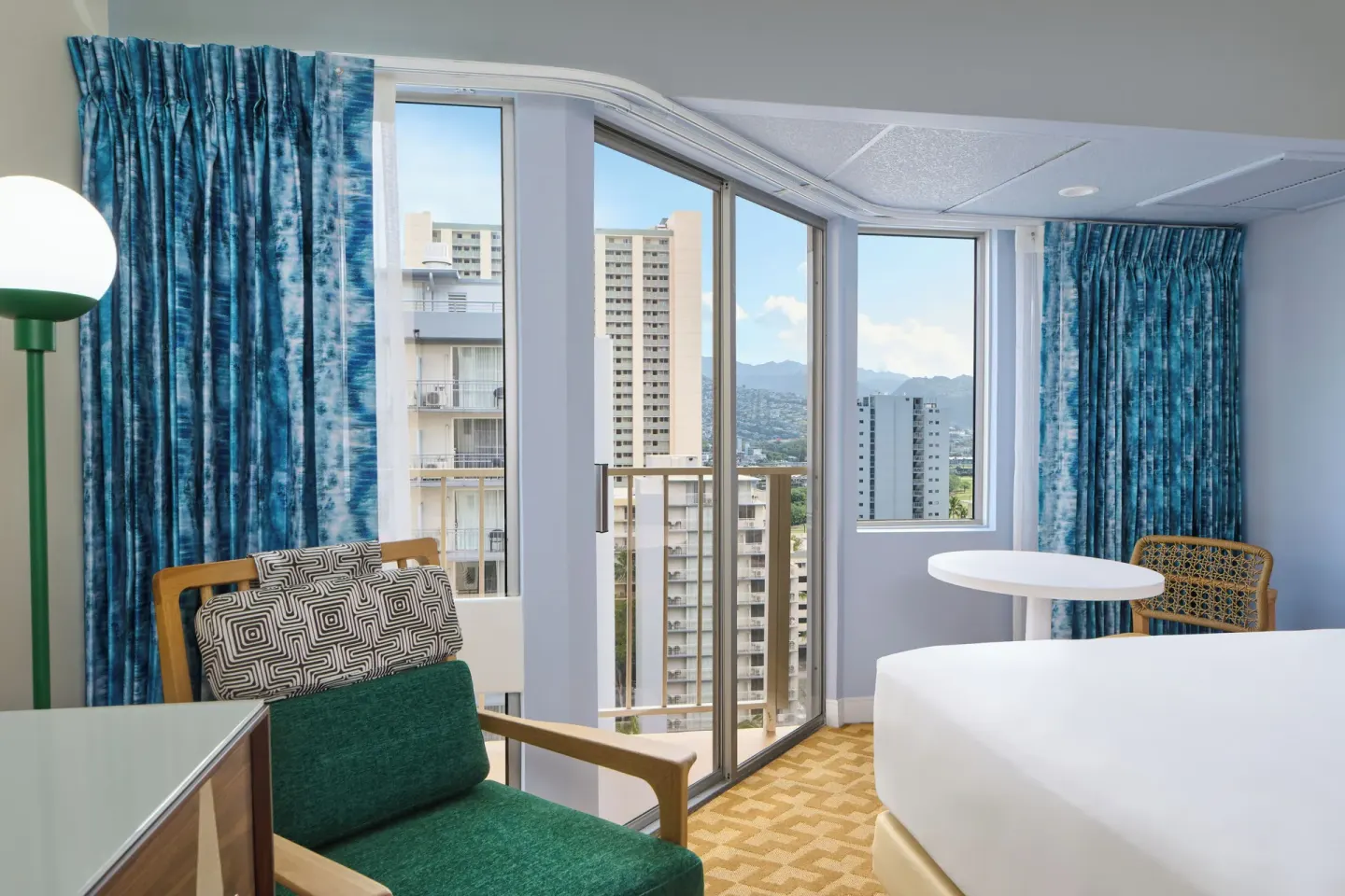 City View room seating area with balcony doors, blue curtains, and skyline view at Waikiki Malia.
