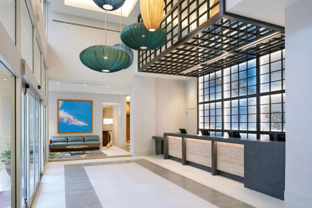 Waikiki Malia lobby with reception desk, tall windows, pendant lights, and seating.