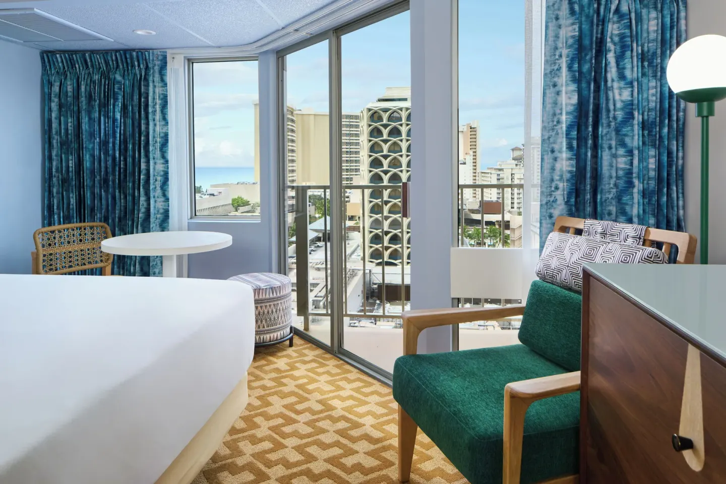 Partial Ocean View room corner with bed, table, chair, and windows at Waikiki Malia.